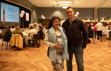 2V9A0019 Expectant mother and her husband standing in front of tables.