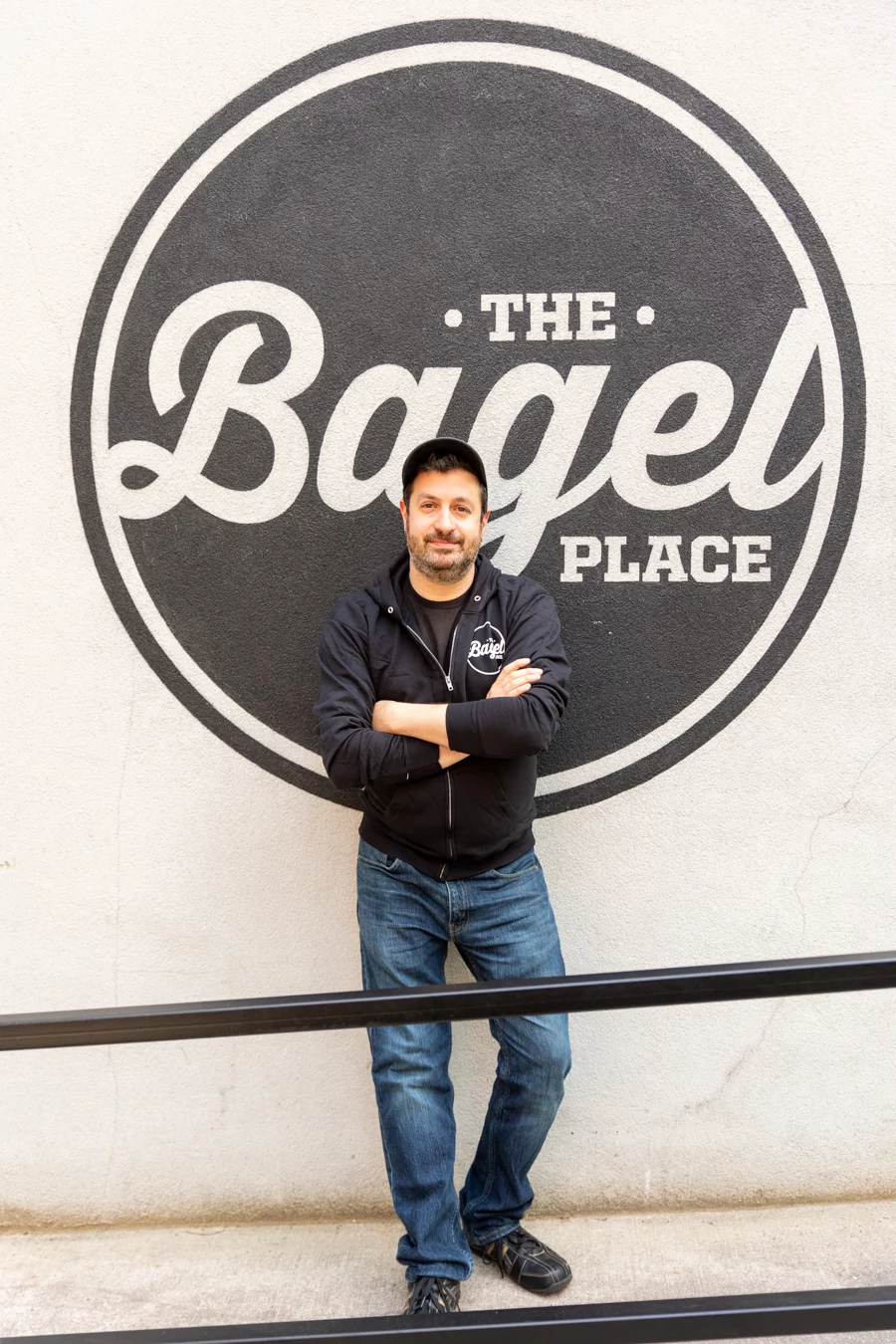 9I4A2100 Man standing in front of The Bagel Place sign.
