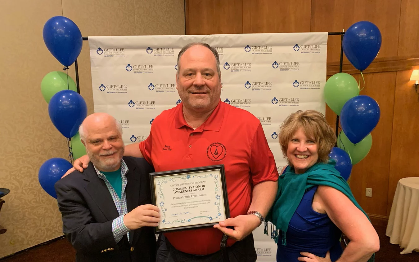 Man being awarded "Community Donor Awareness Award" surrounded by two other people.