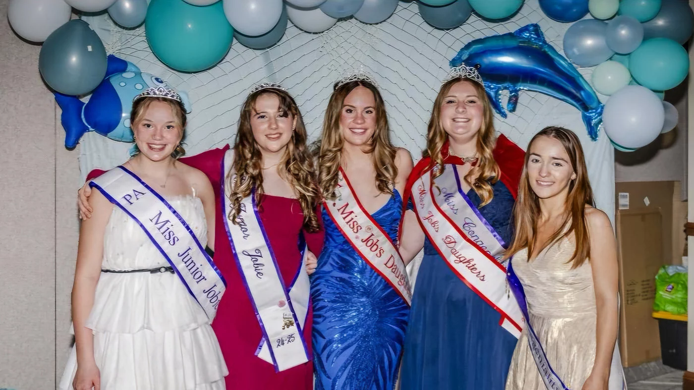 Group of smiling girls in dresses with ocean themed background behind them.