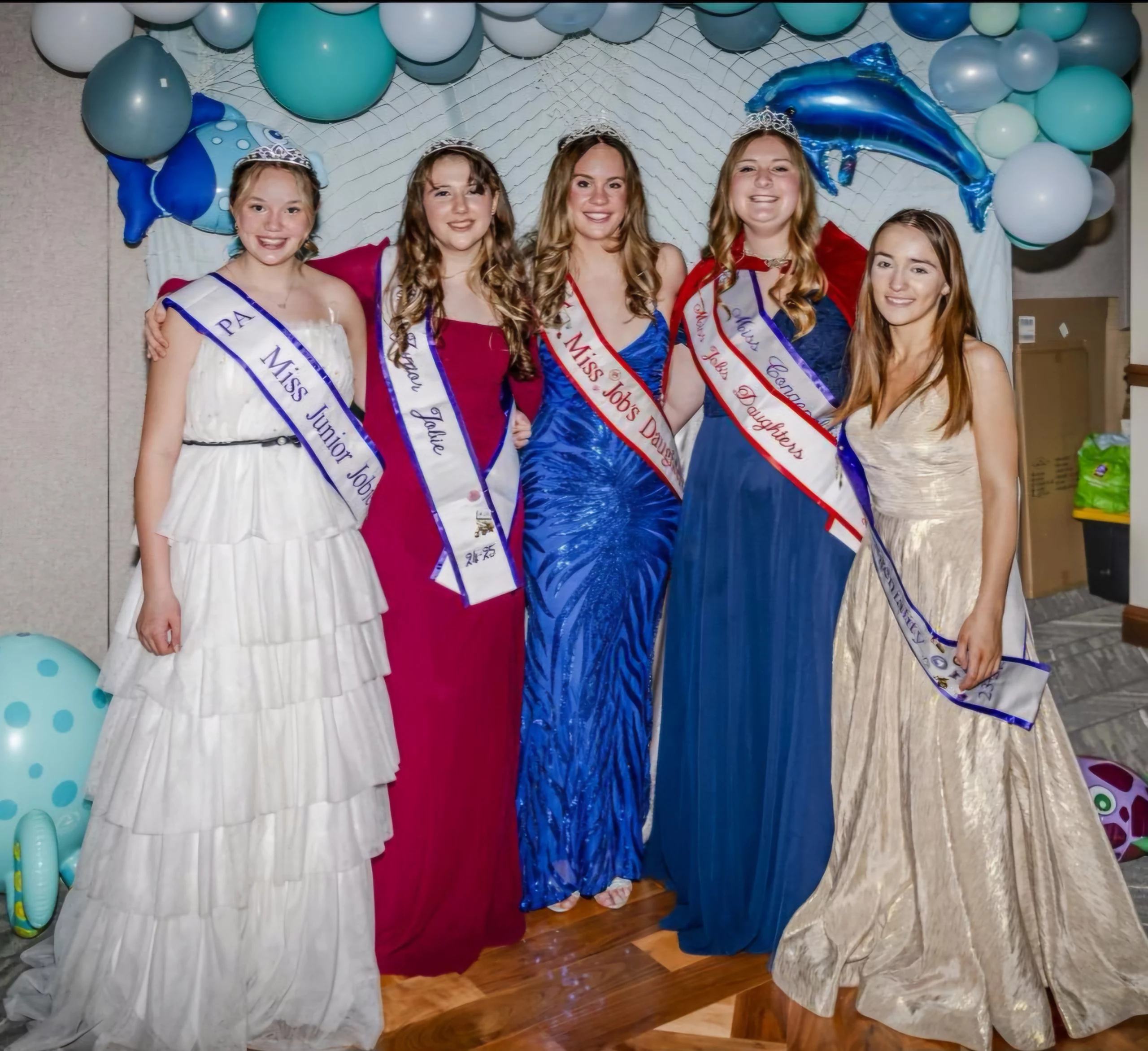 Misses Group of smiling girls in dresses with ocean themed background behind them.
