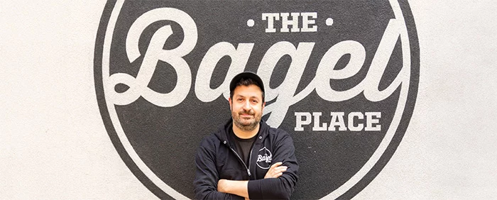 Portrait of man in front of "The Bagel Place" store logo.