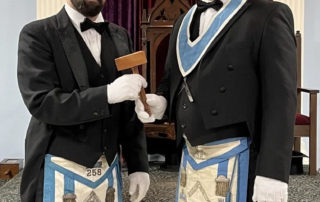 Two masons standing in lodge with gavel.