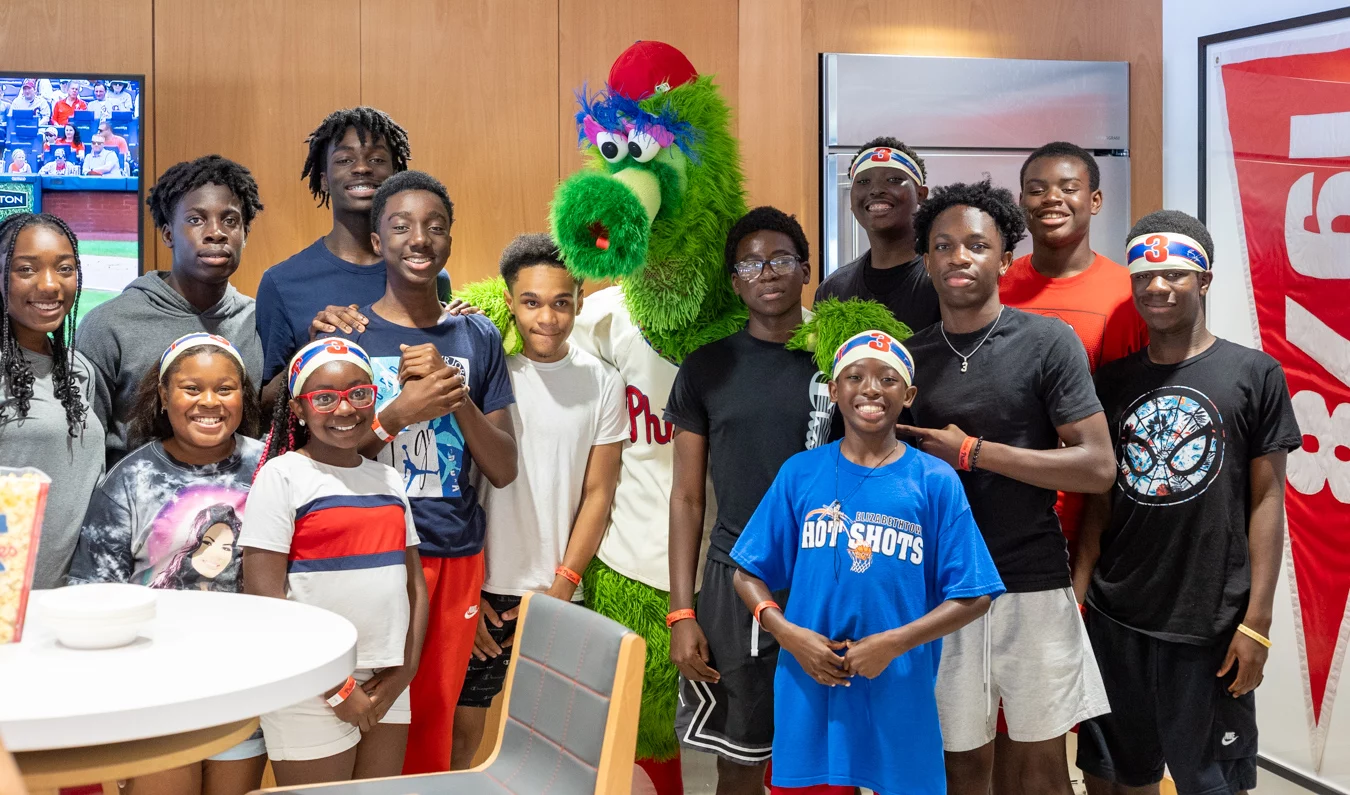 Smiling kids standing with Phillie Phanatic in stadium box.