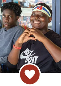 Young boys in baseball stadium, one making a heart with his hands with heart icon.