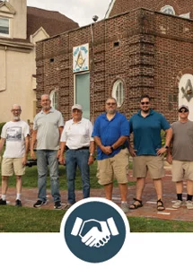 Group of Masons standing in front of their brick lodge building with hand shaking icon.