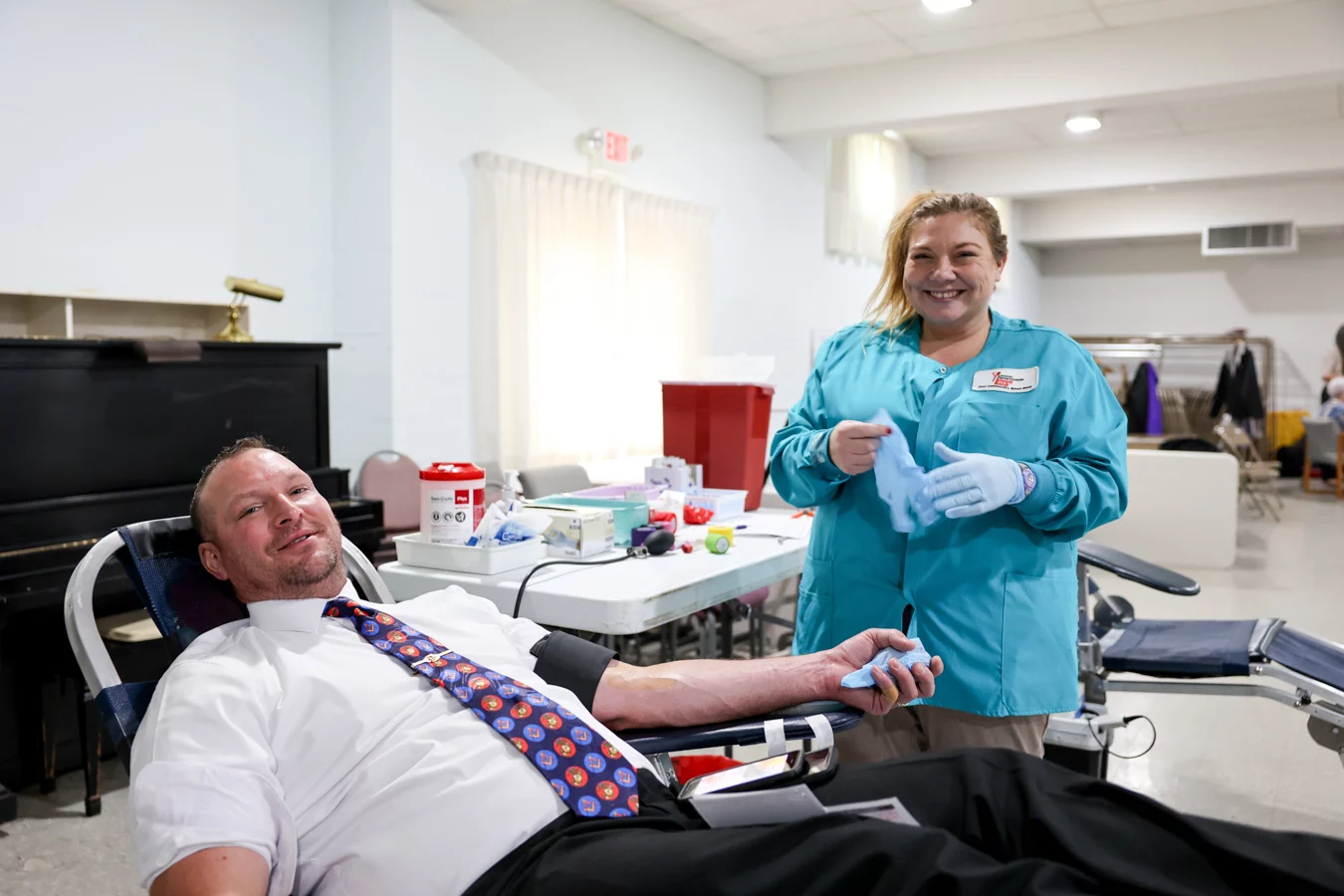 Man smiling while donating blood, smiling technician behind him removing a glove.