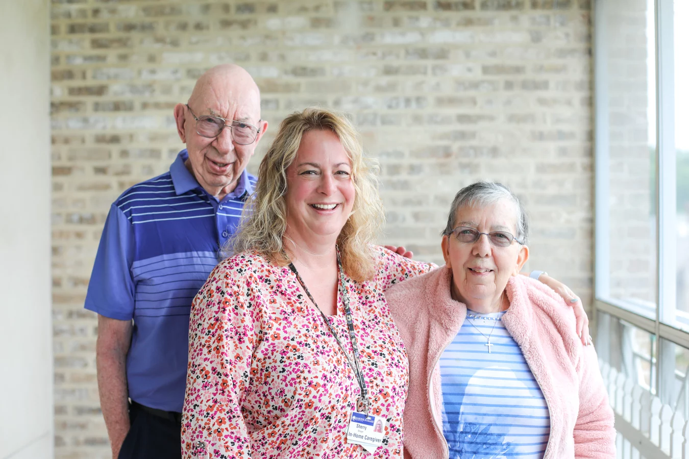 2V9A5467 Smiling elderly couple with staff member standing in the middle with her arm around woman.