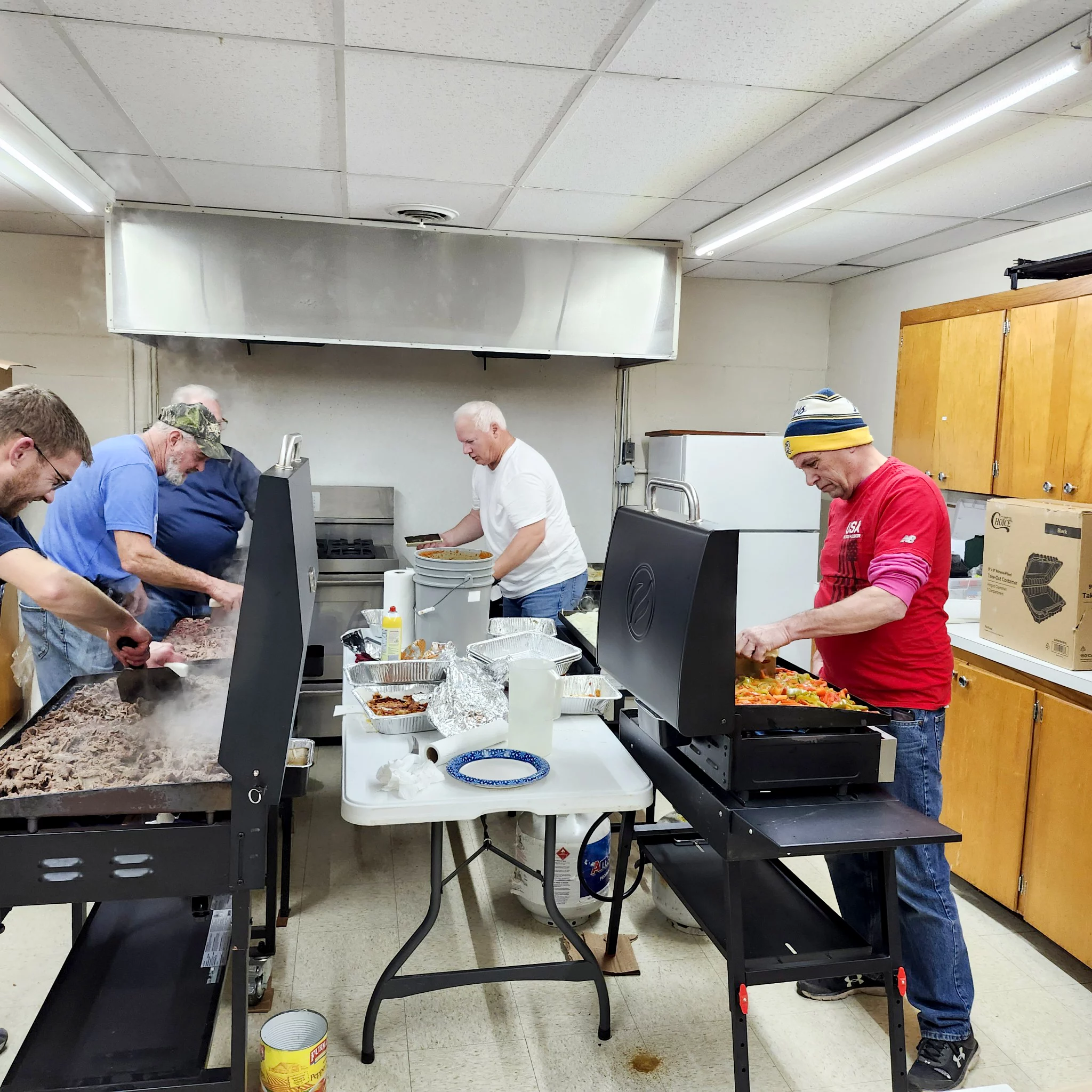 Group of men cooking together in kitchen.