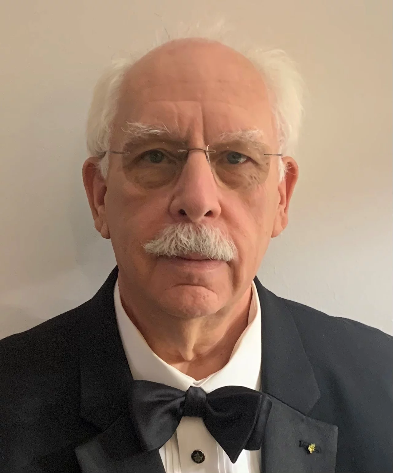 Man in tuxedo with white hair, mustache and glasses.