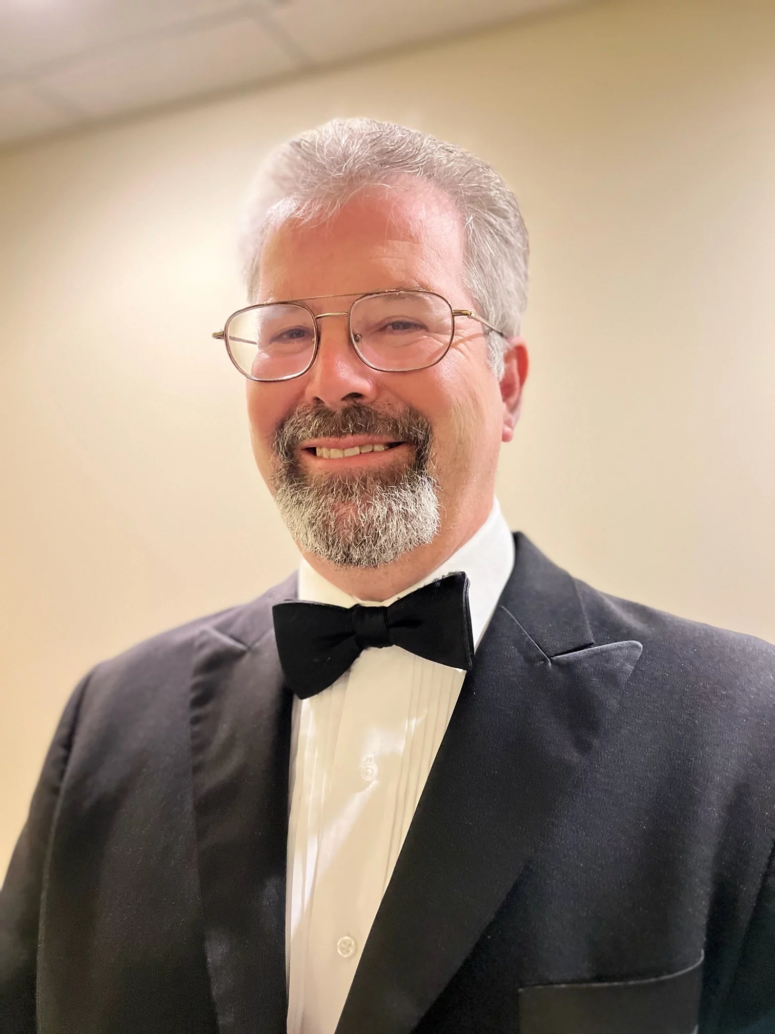 Man in tuxedo with glasses, short white hair and goatee.