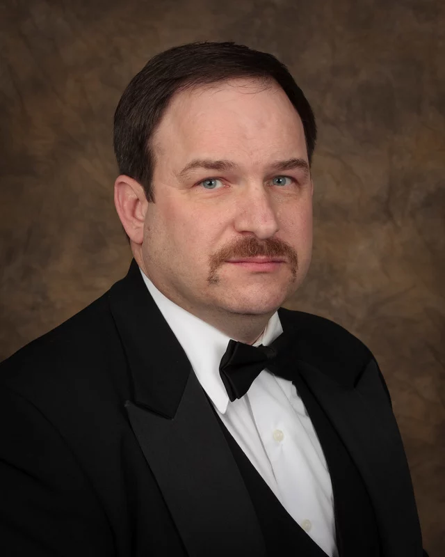 Man in tuxedo with short brown hair and mustache.