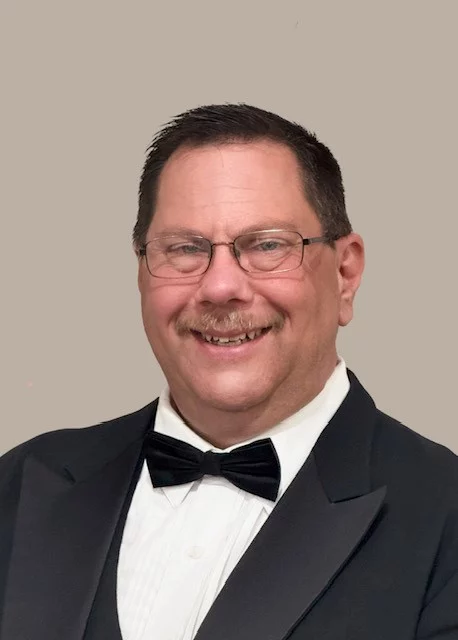 Man in tuxedo with glasses, short brown hair and mustache.