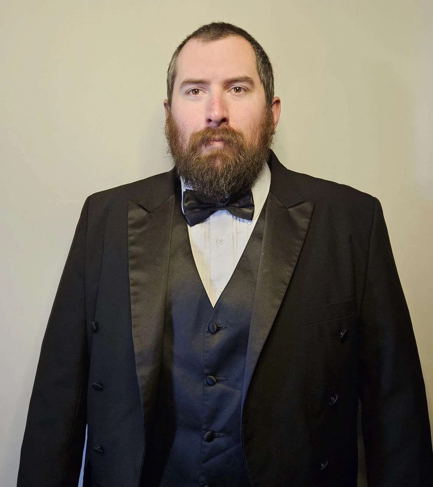 Man with short brown hair and beard in tuxedo.