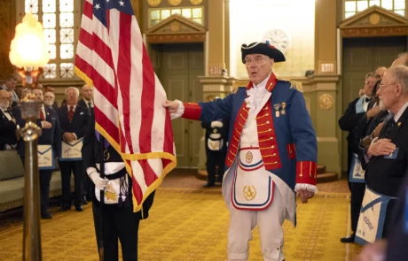 Man dressed in revolutionary war attire holding edge of United States flag.