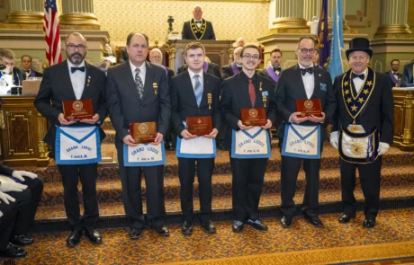 Group of men holding up awards while standing in an ornate hall.
