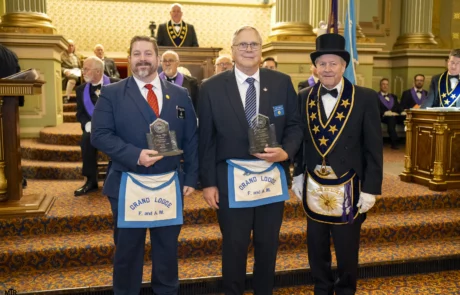 Two men holding awards and standing with Grand Master Larry Derr.