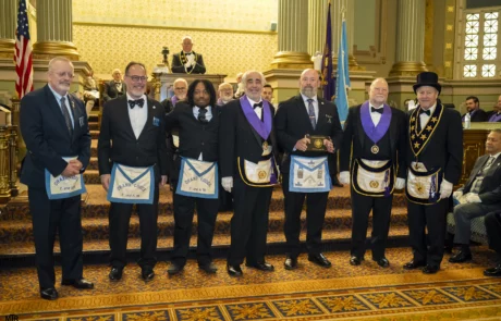 Group of men dressed in regalia and standing in an ornate hall.