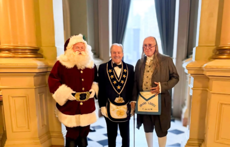 Grandmaster Larry Derr standing with men dressed as Santa Claus and Benjamin Franklin.