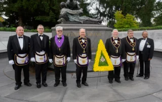 Group of smiling men with Masonic-themed wreath in front of Friend to Friend statue.