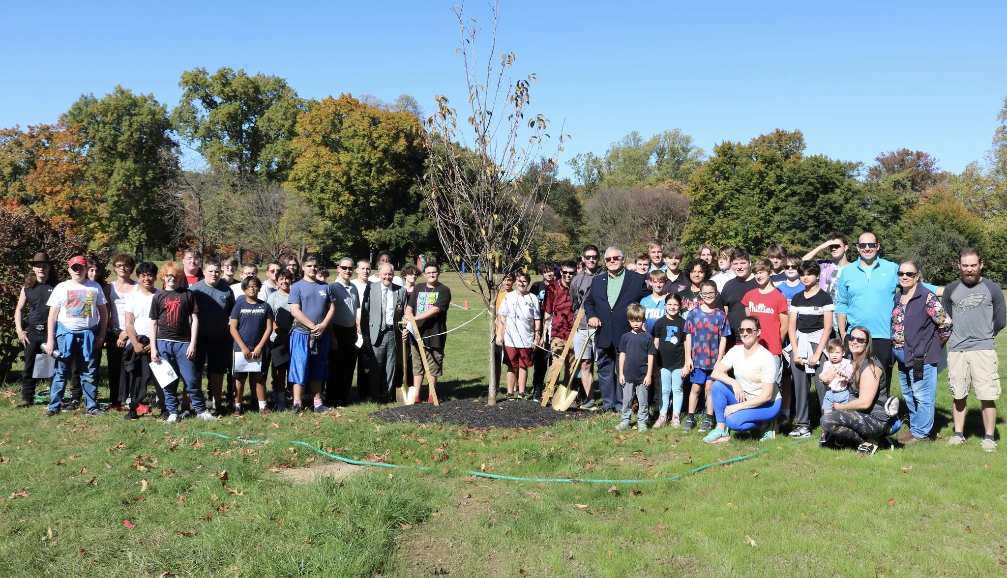 Large group standing around newly-planted tree.