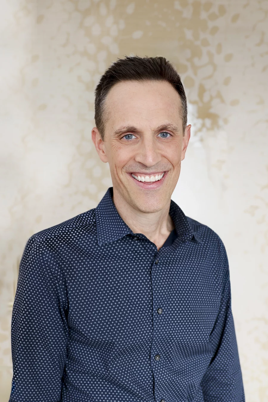1W8A8249-Edit Headshot of smiling man in front of cream background.