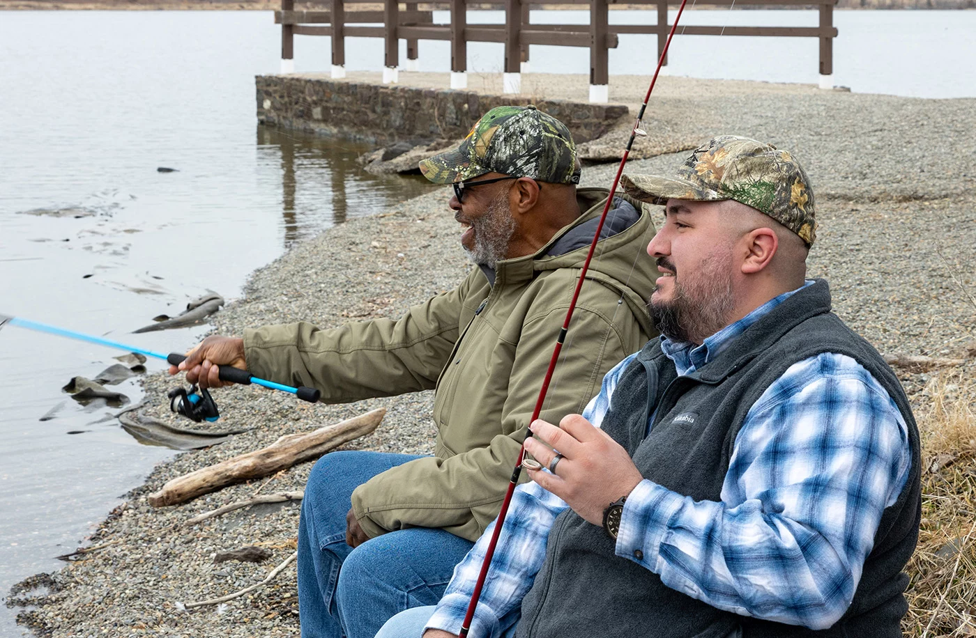 Smiling men fishing together outdoors.