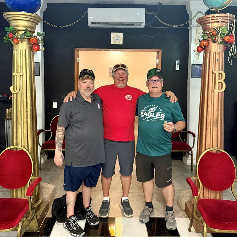 4 Group of three smiling men with red chairs and large pillars to either side of them.