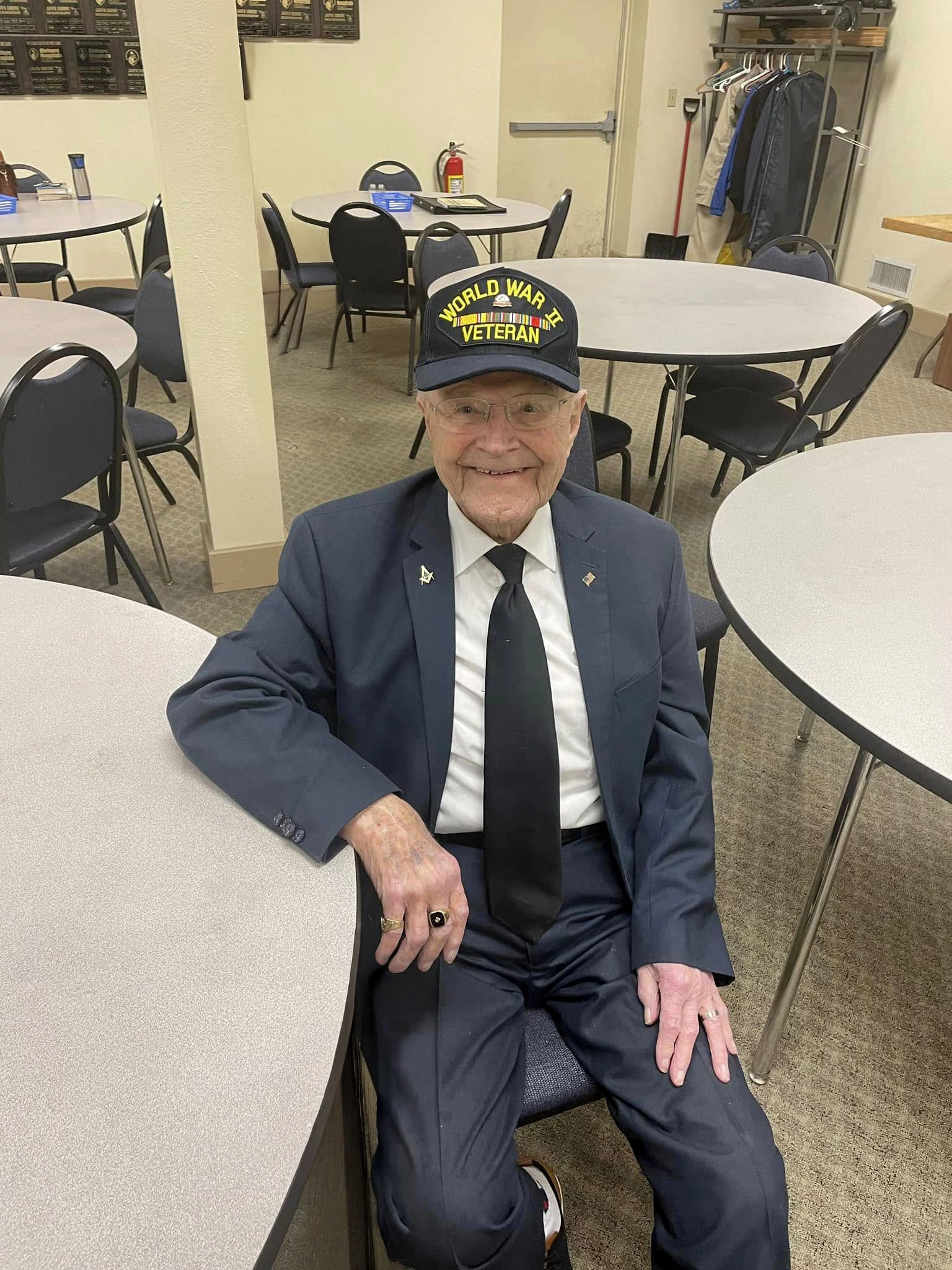 Smiling man in suit sitting at table with World War II Veteran hat.