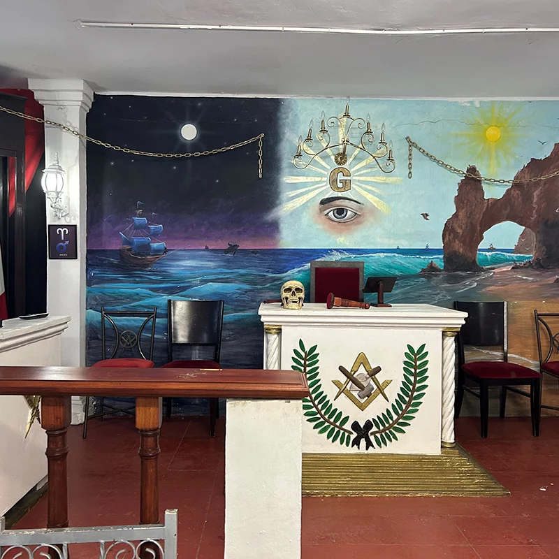 6 Ornate room with masonic-themed mural behind white desk with square and compass design.