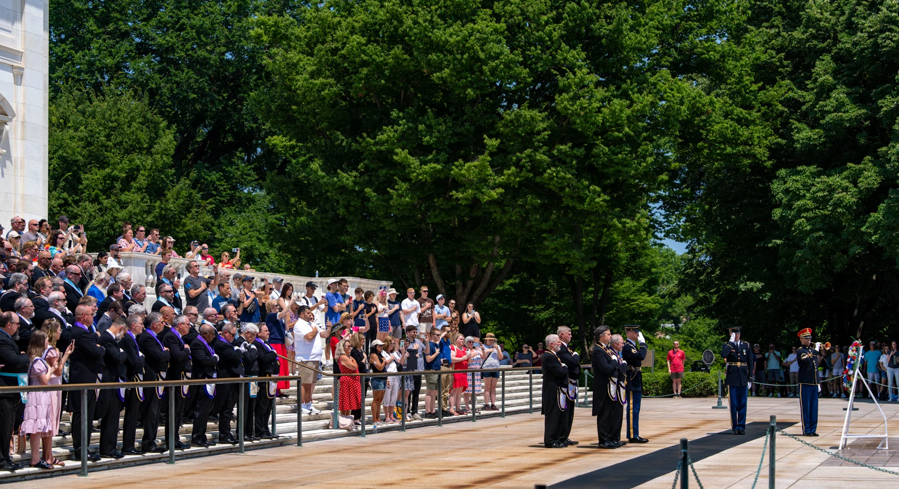 _7R50075 Wide shot of wreath laying at the Tomb of the Unknown Soldier. Grand lodge officers stand in front of the wreath with hands over their hearts while men in masonic dress and mixed group of people stand behind them.