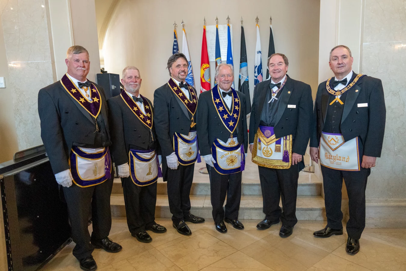 DSC07606_edited_FINAL Grand Lodge officers in masonic dress standing with multiple flags behind them.