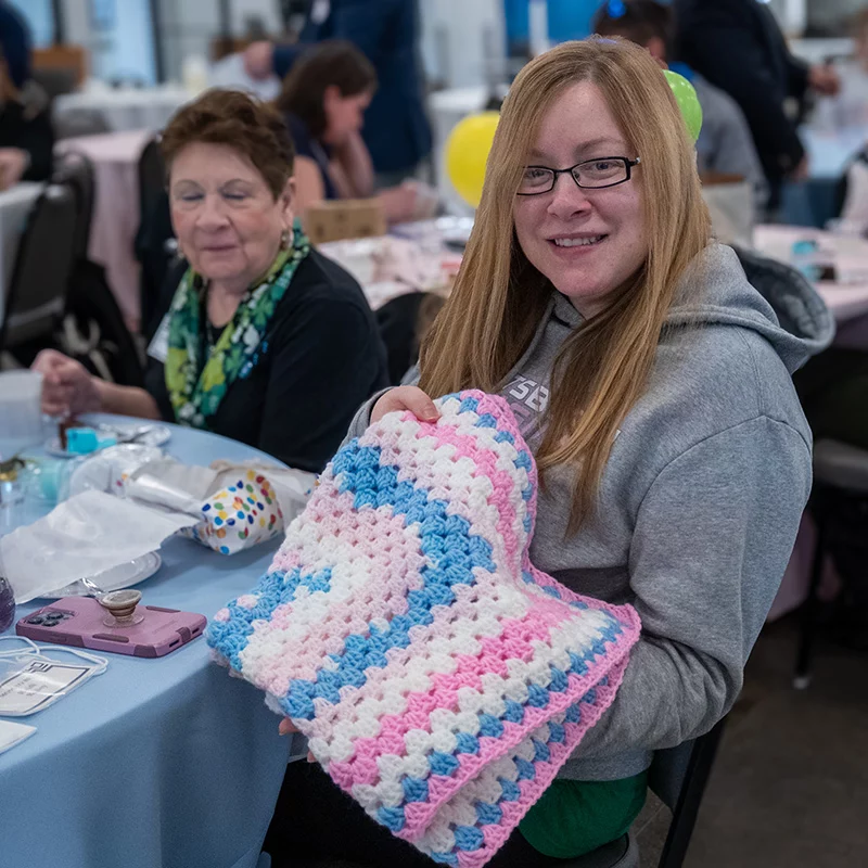 LZ3_3050 Smiling woman holding up colorful baby blanket.