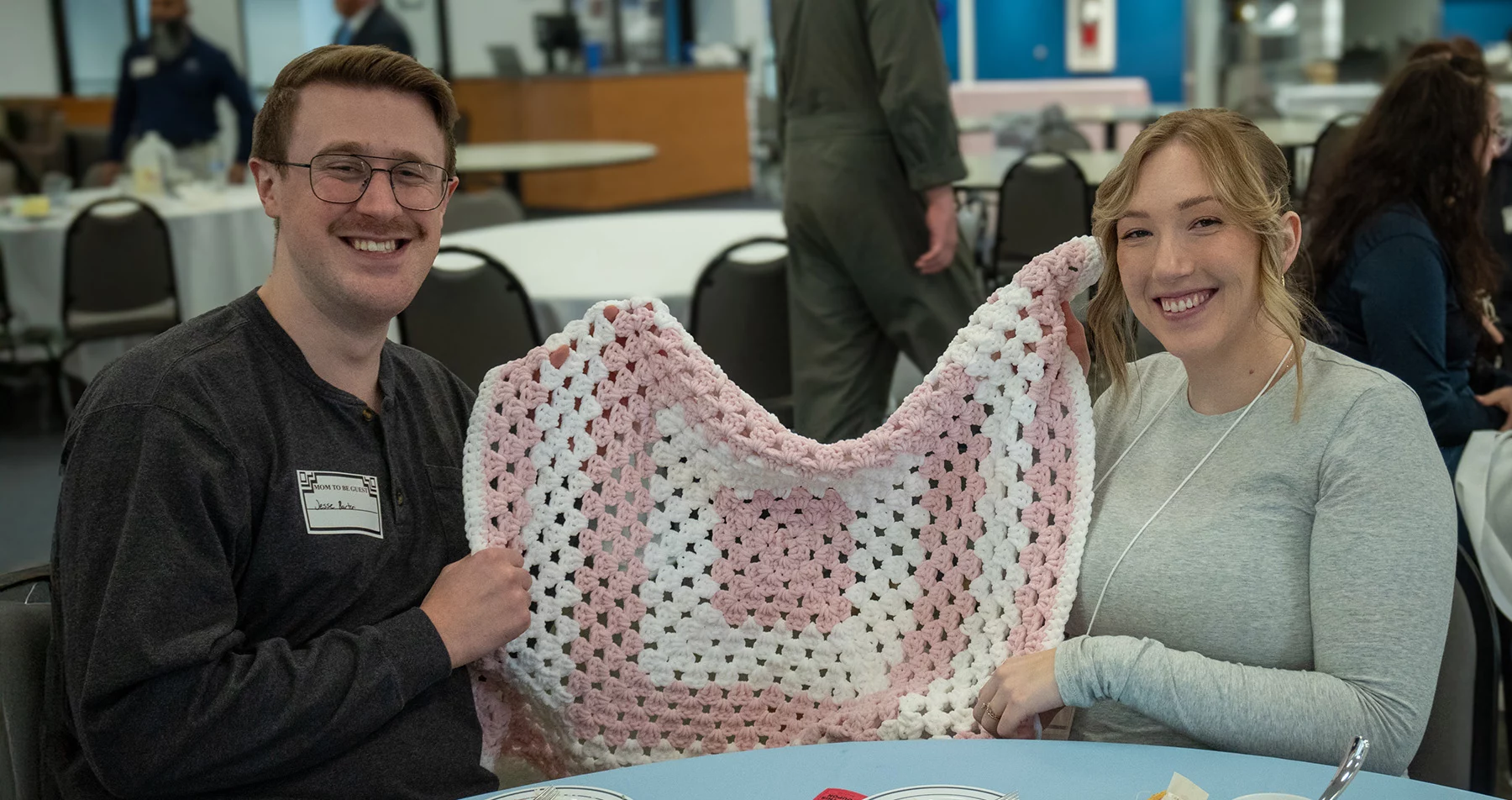 Smiling couple holding up baby blanket.