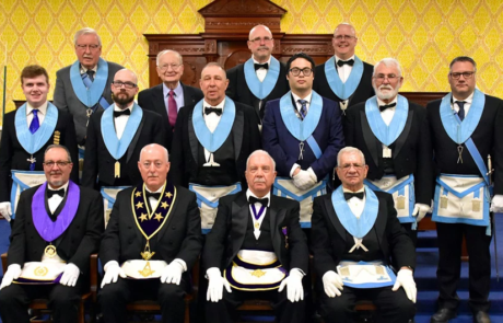 Group of men in Masonic dress seated and standing in lodge room.