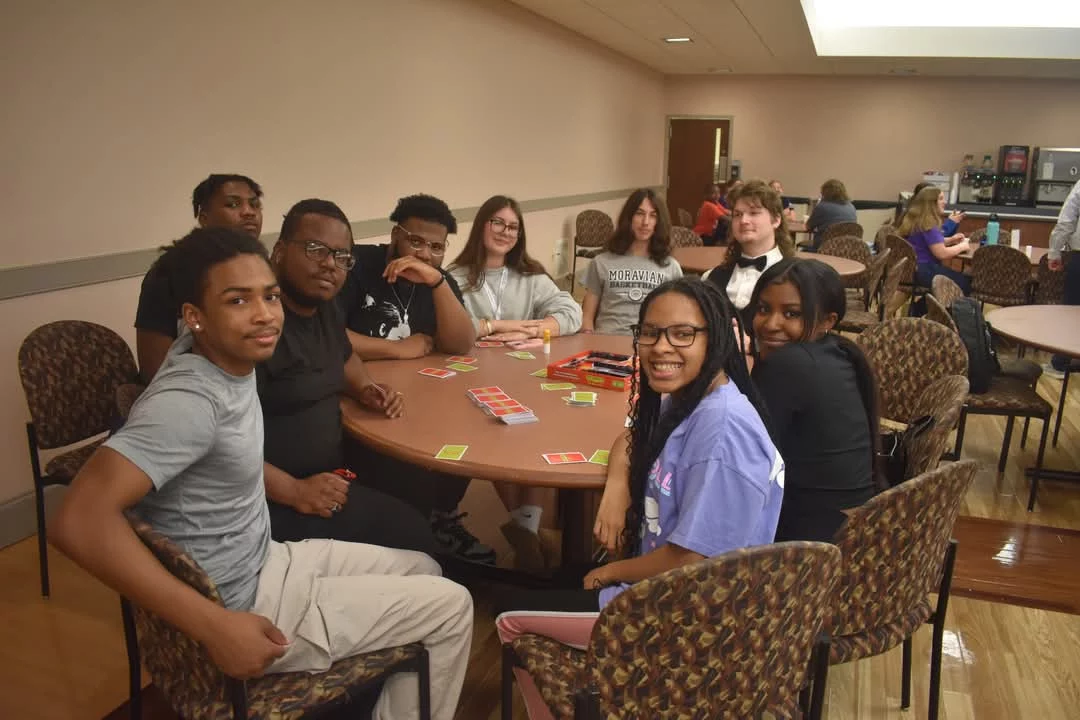 Power Five Photo 2 Smiling group of teens playing card game at table.
