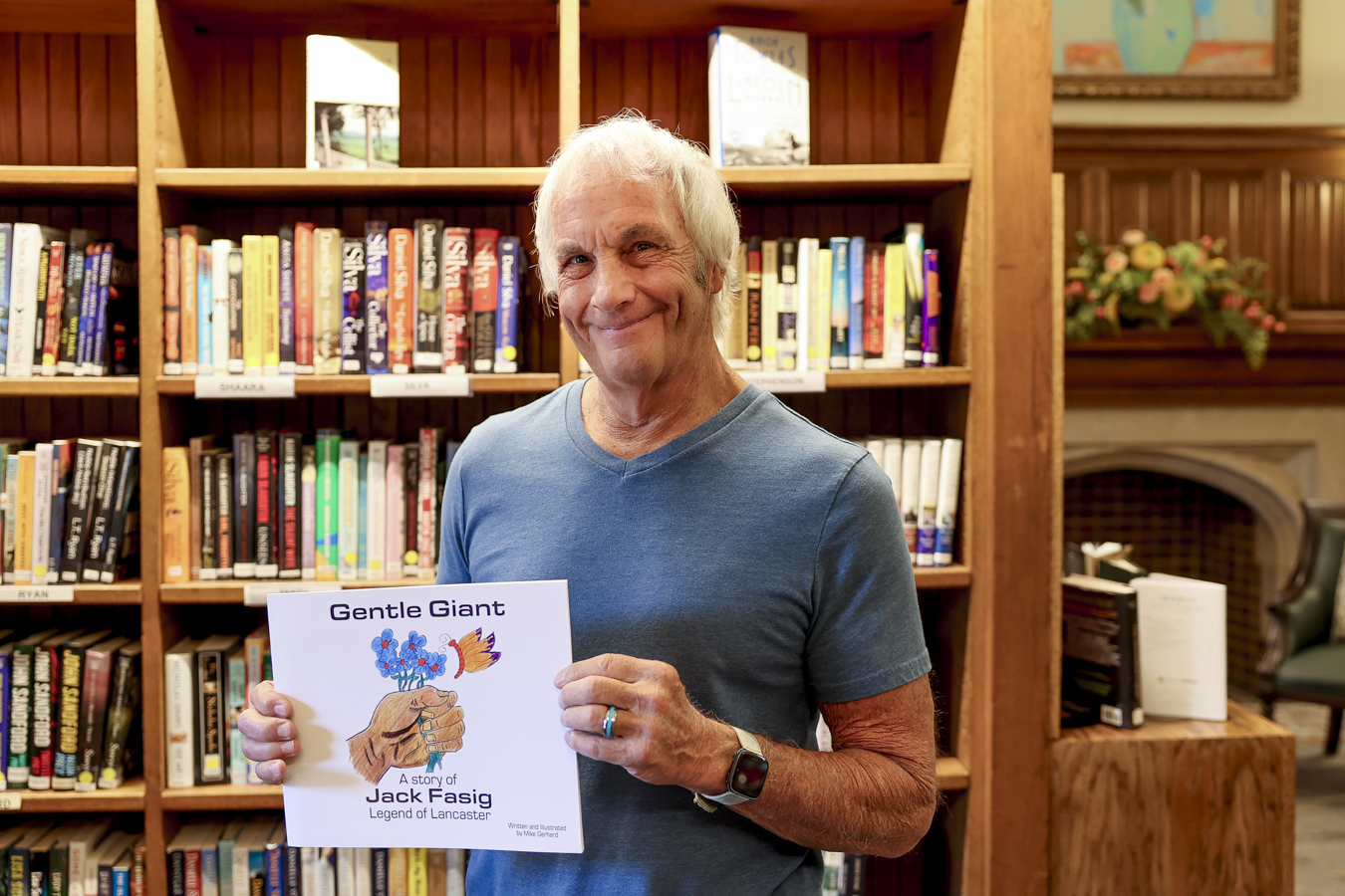 Smiling man holding "Gentle Giant" book in cozy library setting.