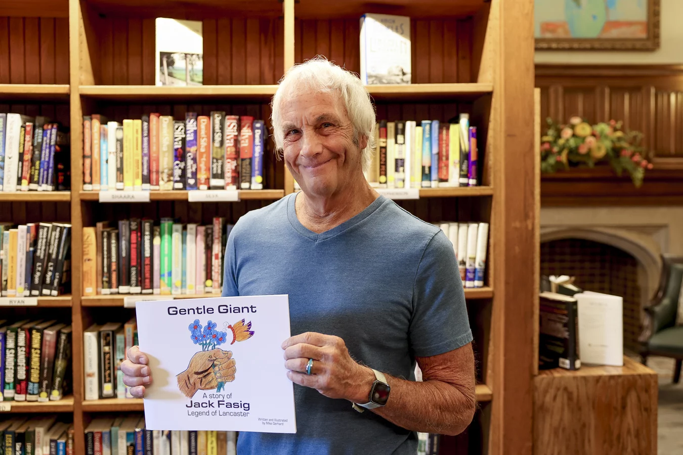 Smiling man holding "Gentle Giant" book in cozy library setting.