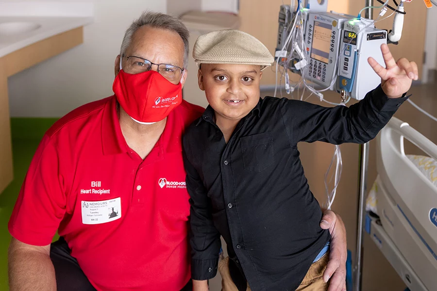 Smiling man in mask and boy standing together in front of medical equipment.