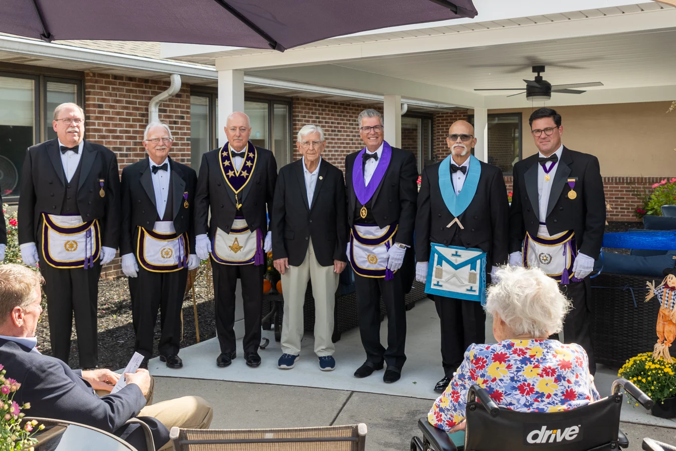 Group of men in Masonic dress standing under pavilion in front of audience.