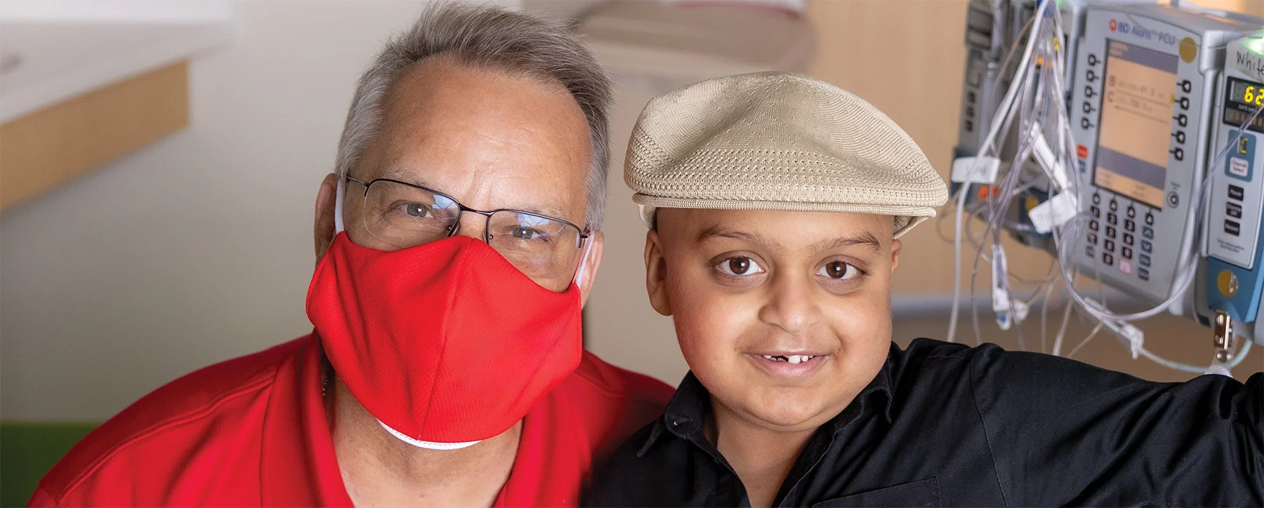 Man wearing mask and smiling boy with medical equipment in the background.