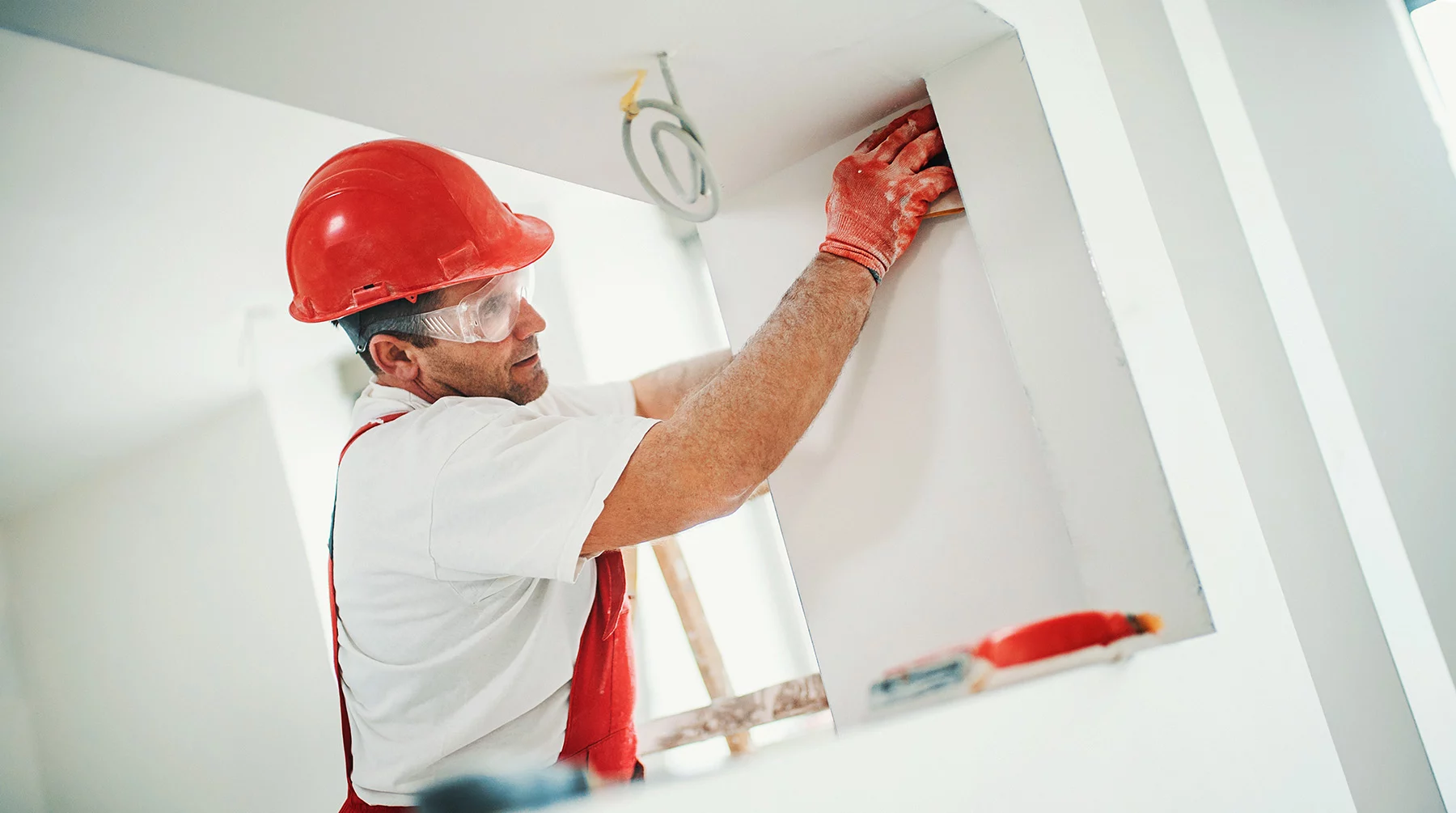 Man in construction hat and gloves sanding drywall.