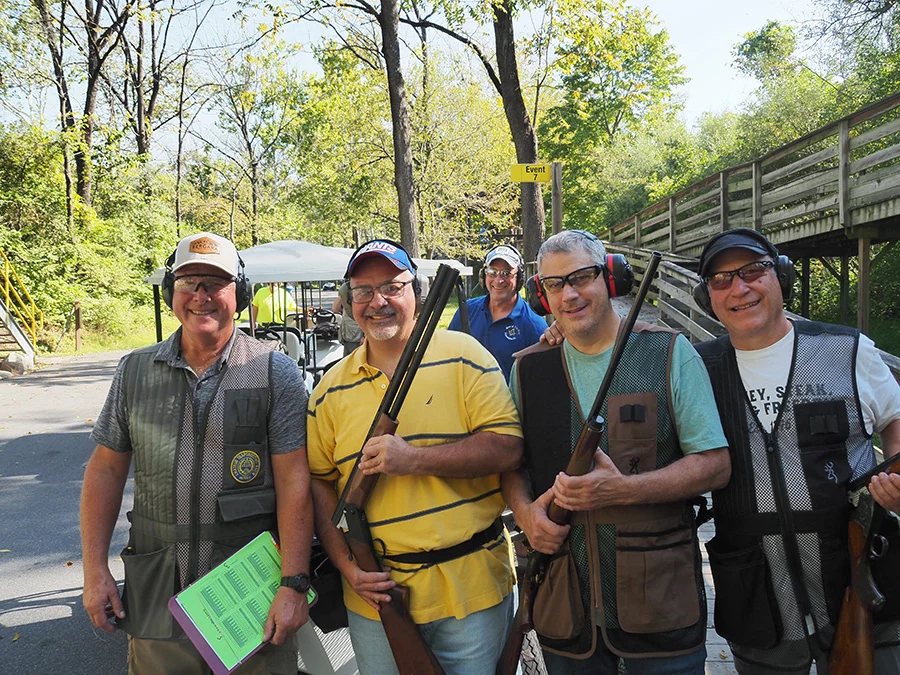 Men in vests wearing ear protection and holding rifles.