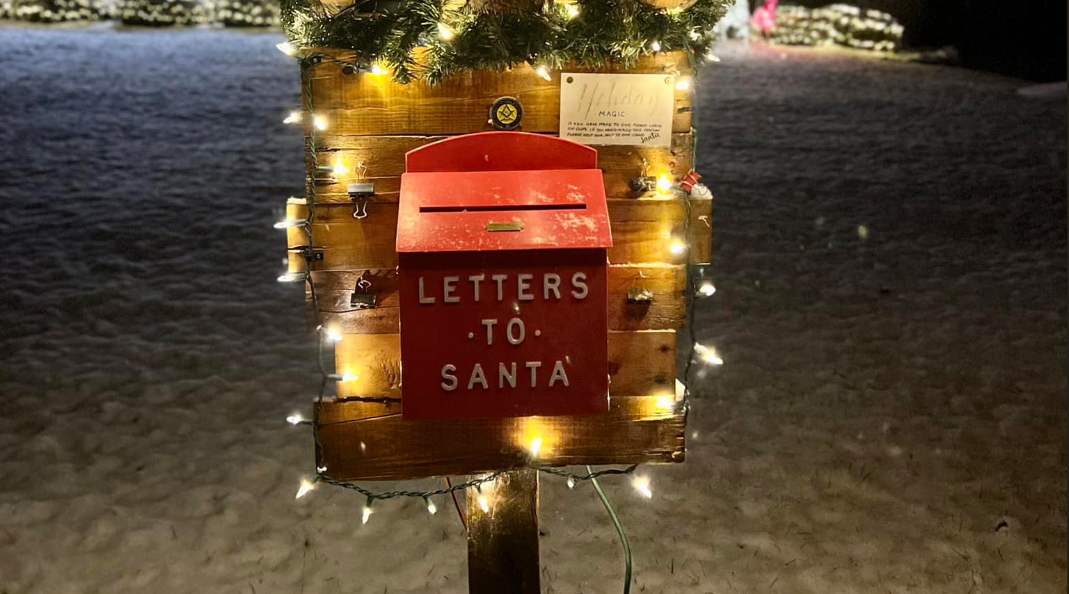 Illuminated post with mailbox labeled "letters to Santa" surrounded by snow