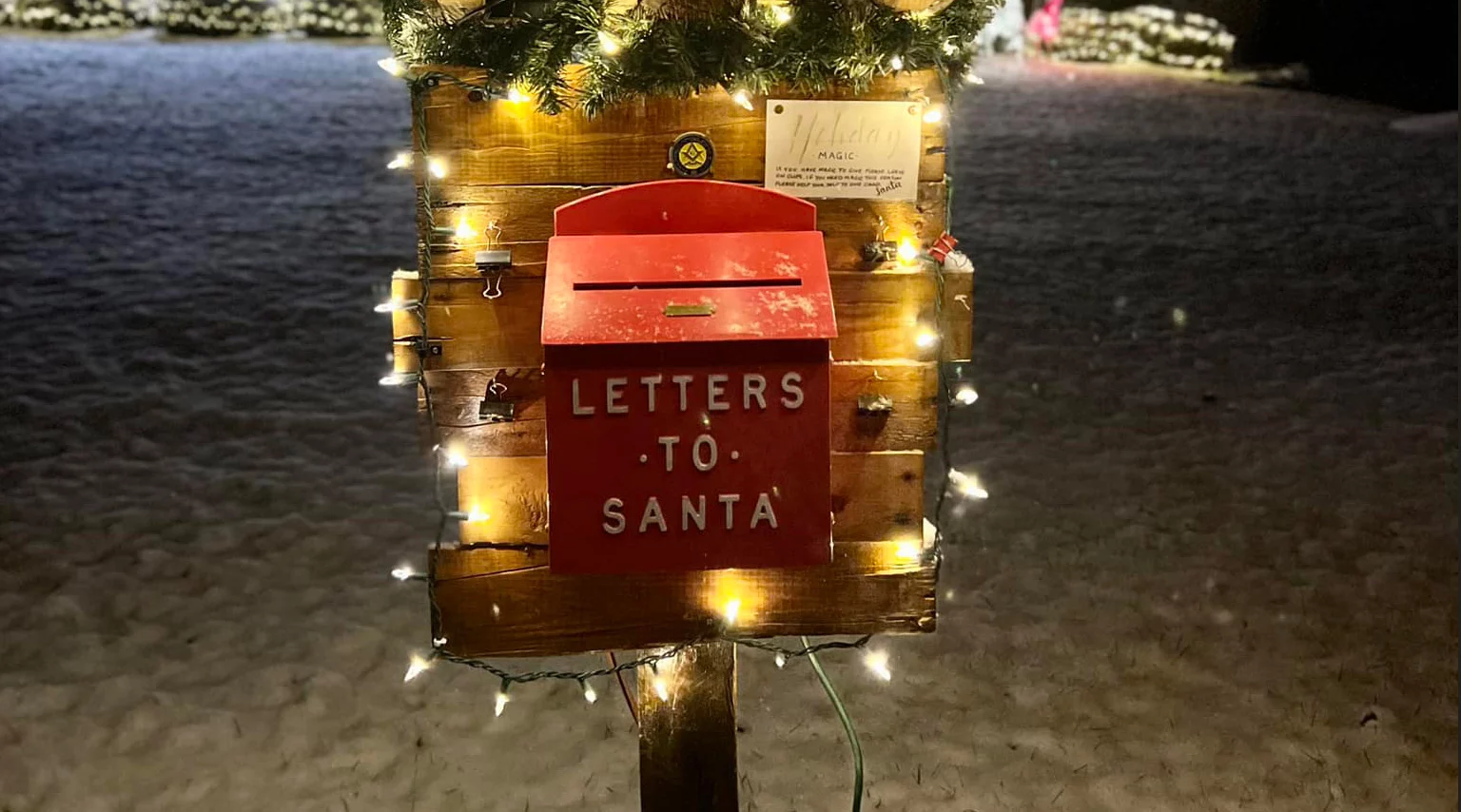Illuminated post with mailbox labeled "letters to Santa" surrounded by snow.