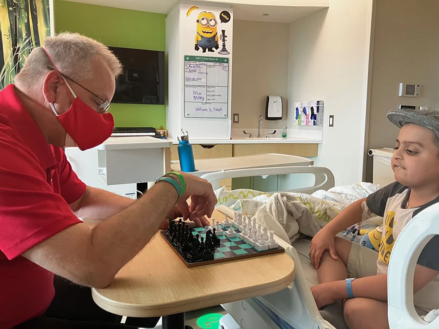 Man playing chess with boy sitting in hospital bed.