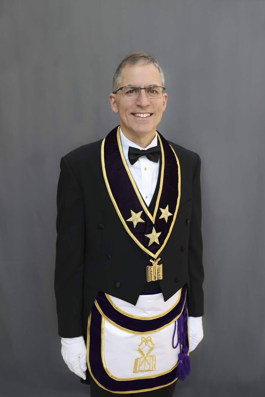 Smiling man with short hair and glasses dressed in Masonic Grand Lodge Officer attire.