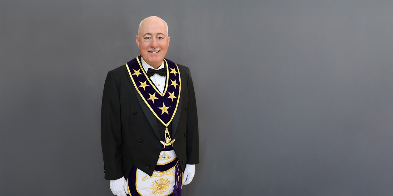 1W8A0477-Edit-Edit Grand Master Robert Brink smiling while dressed in Masonic Grand Lodge Officer attire.