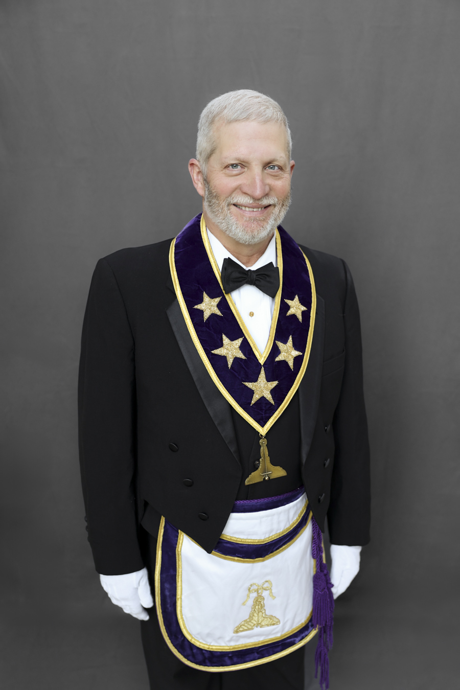 Smiling man with short grey hair and beard dressed in Masonic Grand Lodge Officer attire.