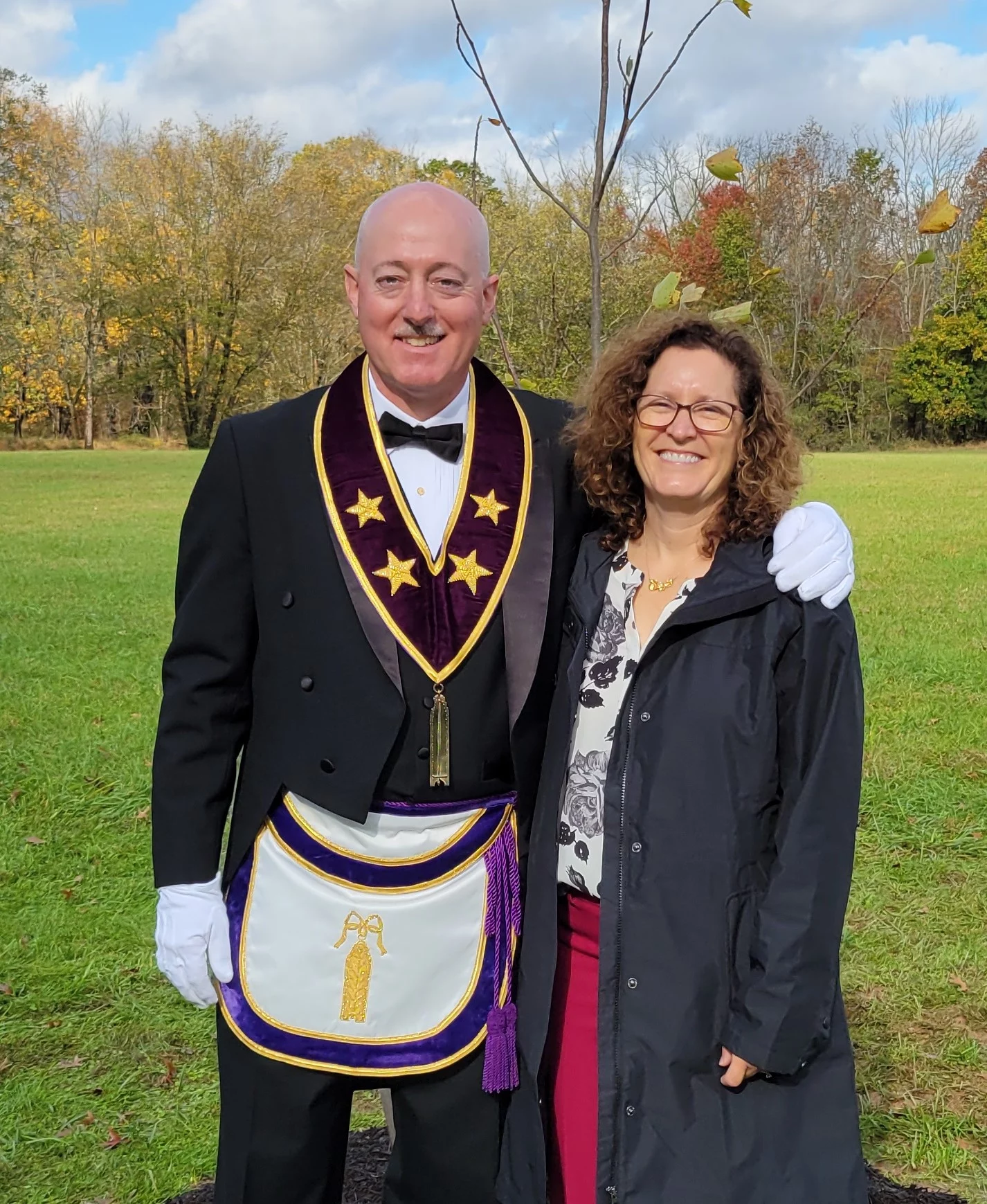 Grand Master Robert Brink, dressed in Masonic attire, with his arm around his wife, both are smiling.